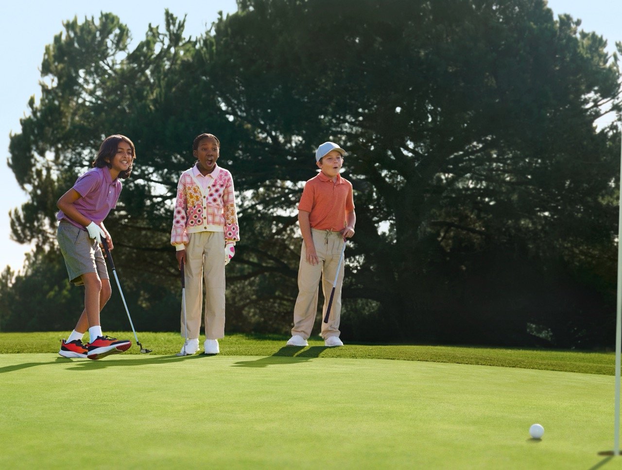 Three happy youth golfers stand on a golf course, clubs in hand, looking surprised by something in the distance