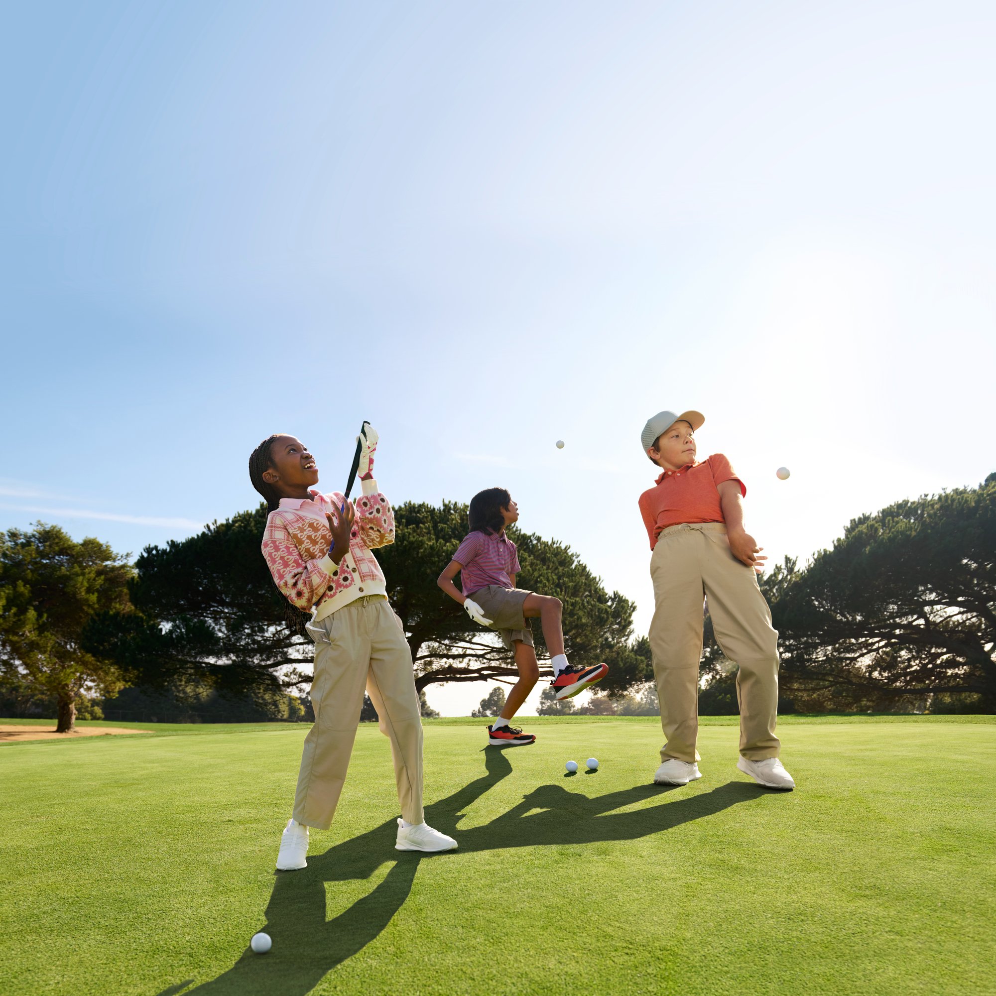 Three youth golfers enjoy themselves on a course while playing around with some golf balls and clubs