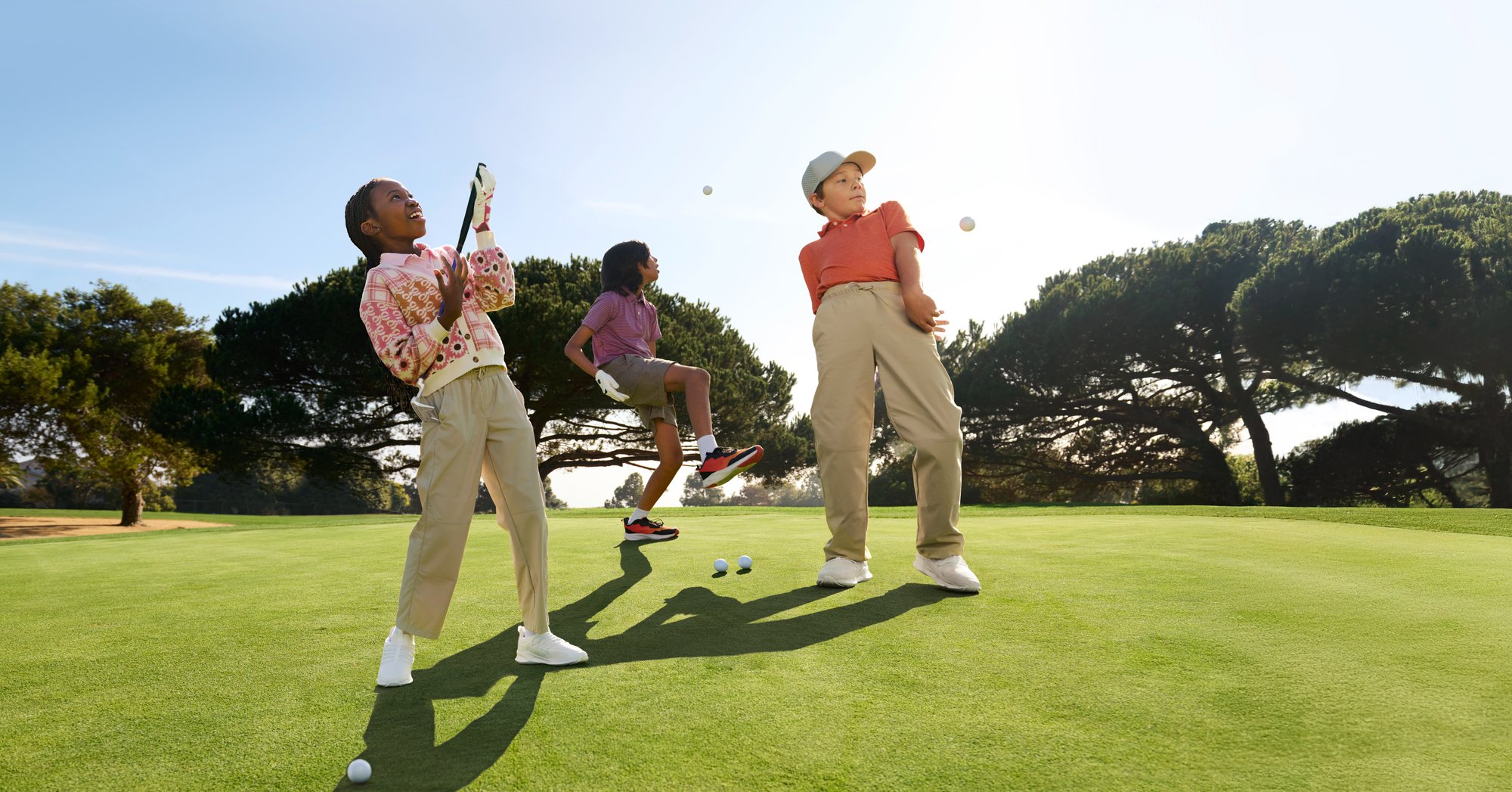 Three youth golfers enjoy themselves on a course while playing around with some golf balls and clubs