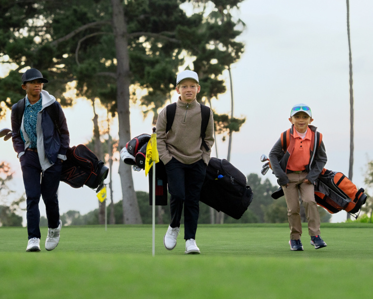 Three young male golf players walk on the fairway of a golf course.